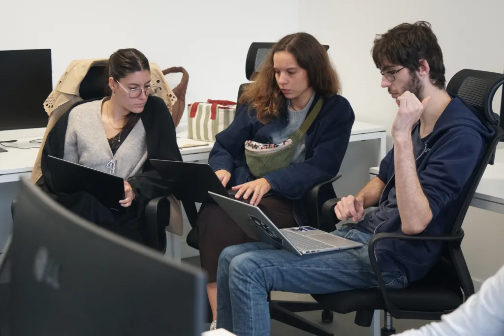Des étudiants collaborent pendant l’exercice de cyberdéfense DefHack 2026 Trois étudiants travaillent sur leurs ordinateurs portables, assis sur des chaises de bureau