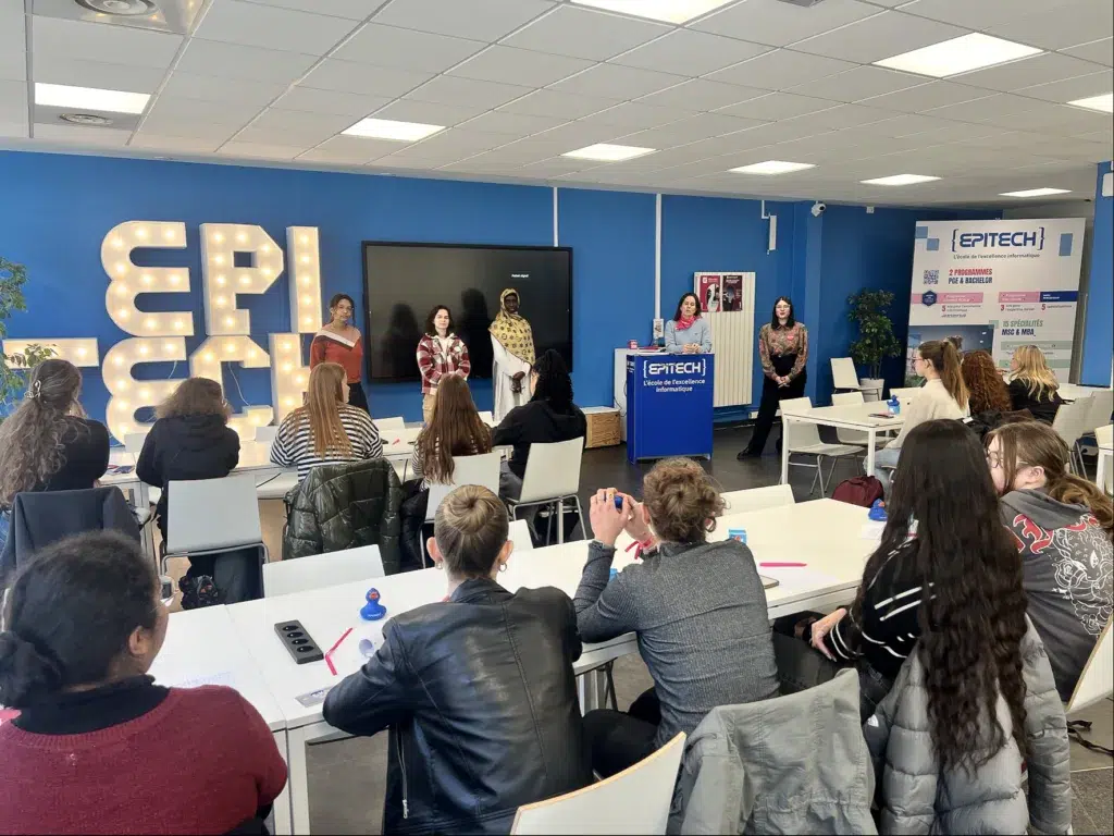 Présentation à l'école EPITECH avec des étudiants assis dans une salle de cours, écoutant des intervenants près d'un pupitre et d'un grand écran.